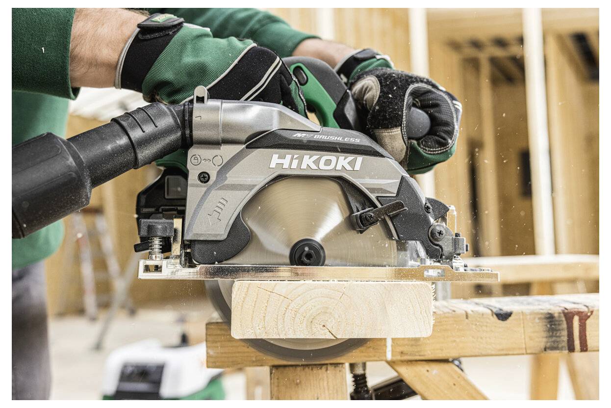 Osoba w odzieży ochronnej używa piły tarczowej Hikoki do cięcia drewnianej deski na koźle warsztatowym w otoczeniu budowy.