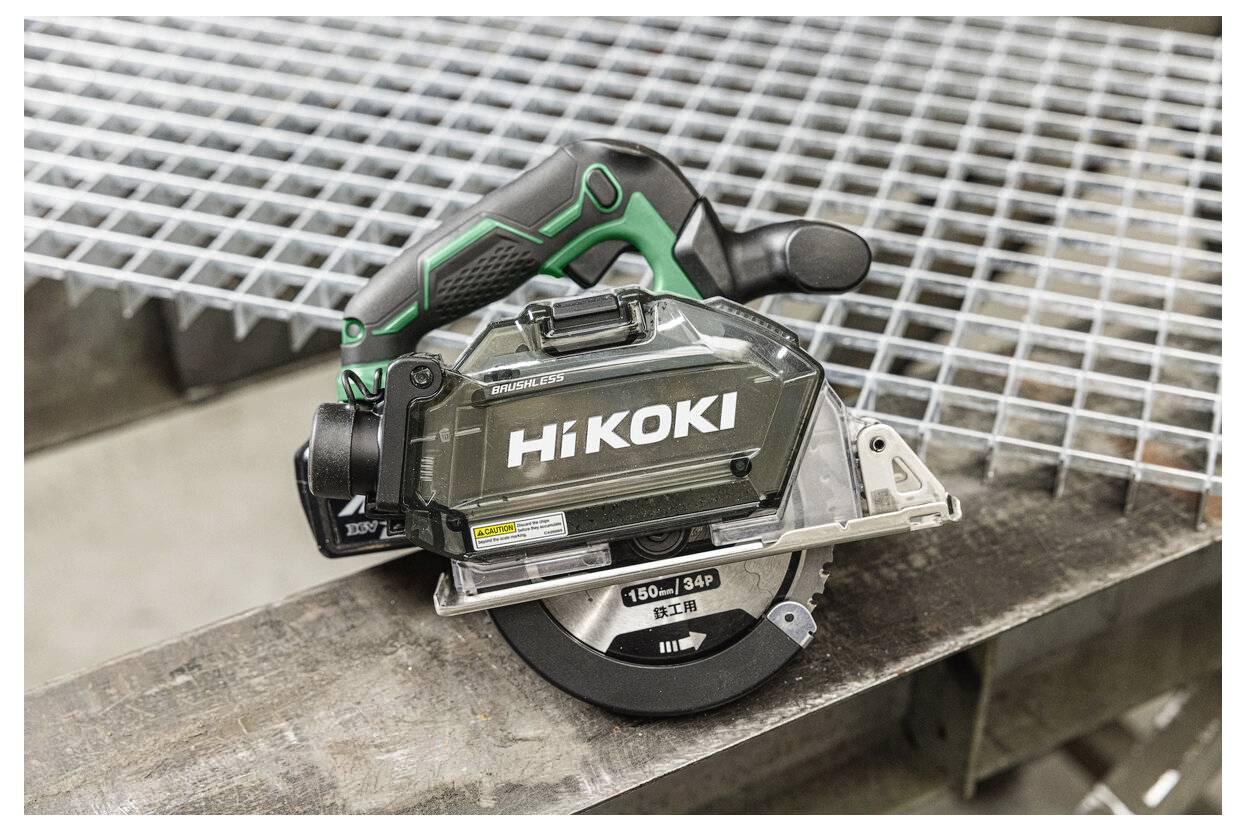 Akumulatorowa piła tarczowa z czarno-zielonym uchwytem, oznaczona marką 'HiKOKI', spoczywa na metalowej kracie, prezentując swoją przenośność i design.