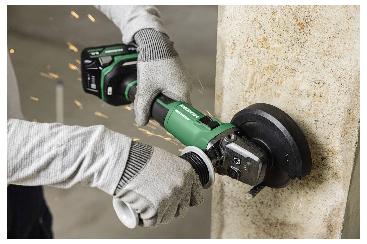 Osoba w rękawicach używa bezprzewodowej szlifierki kątowej do wyrównywania krawędzi powierzchni betonowej, a wokół szlifierki widoczne są iskry.