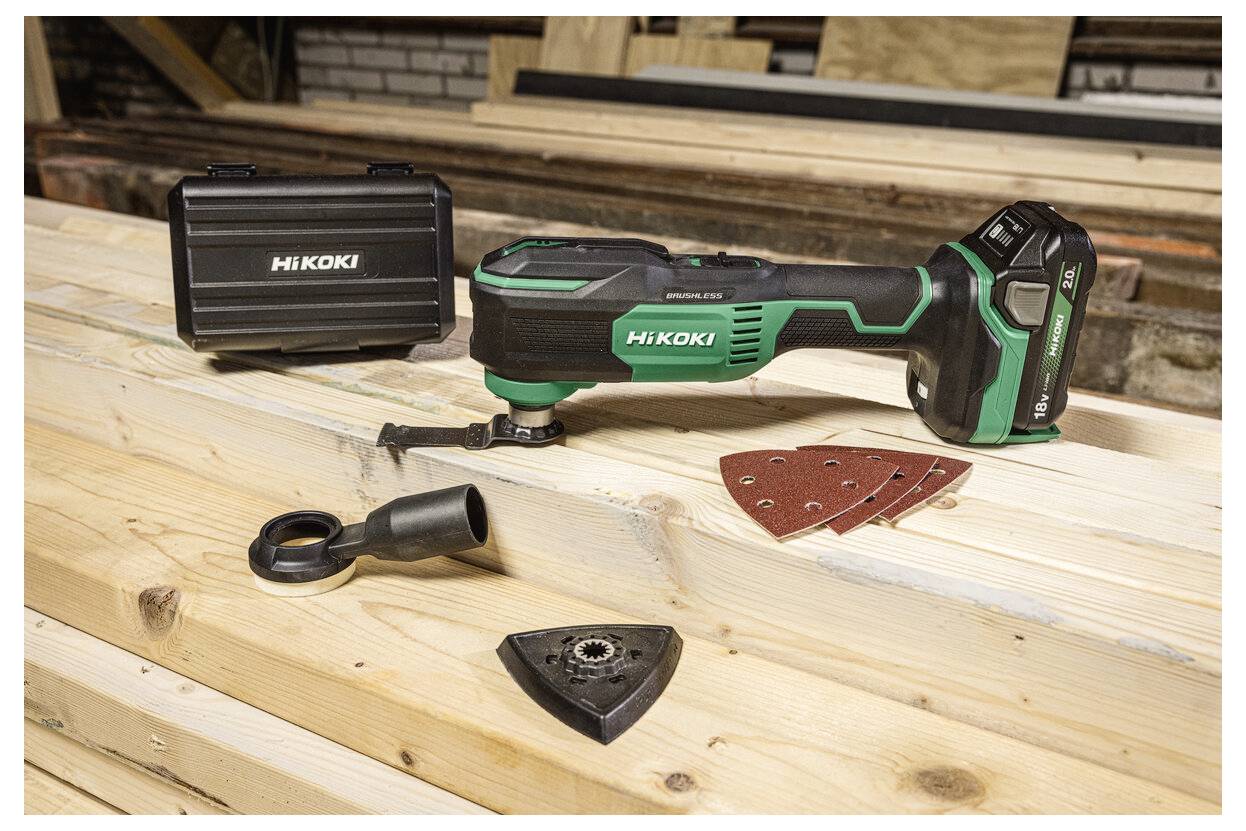 Wielofunkcyjne narzędzie bezprzewodowe z akcesoriami, w tym podkładką do szlifowania i walizką, jest wystawione na drewnianych deskach w warsztacie.