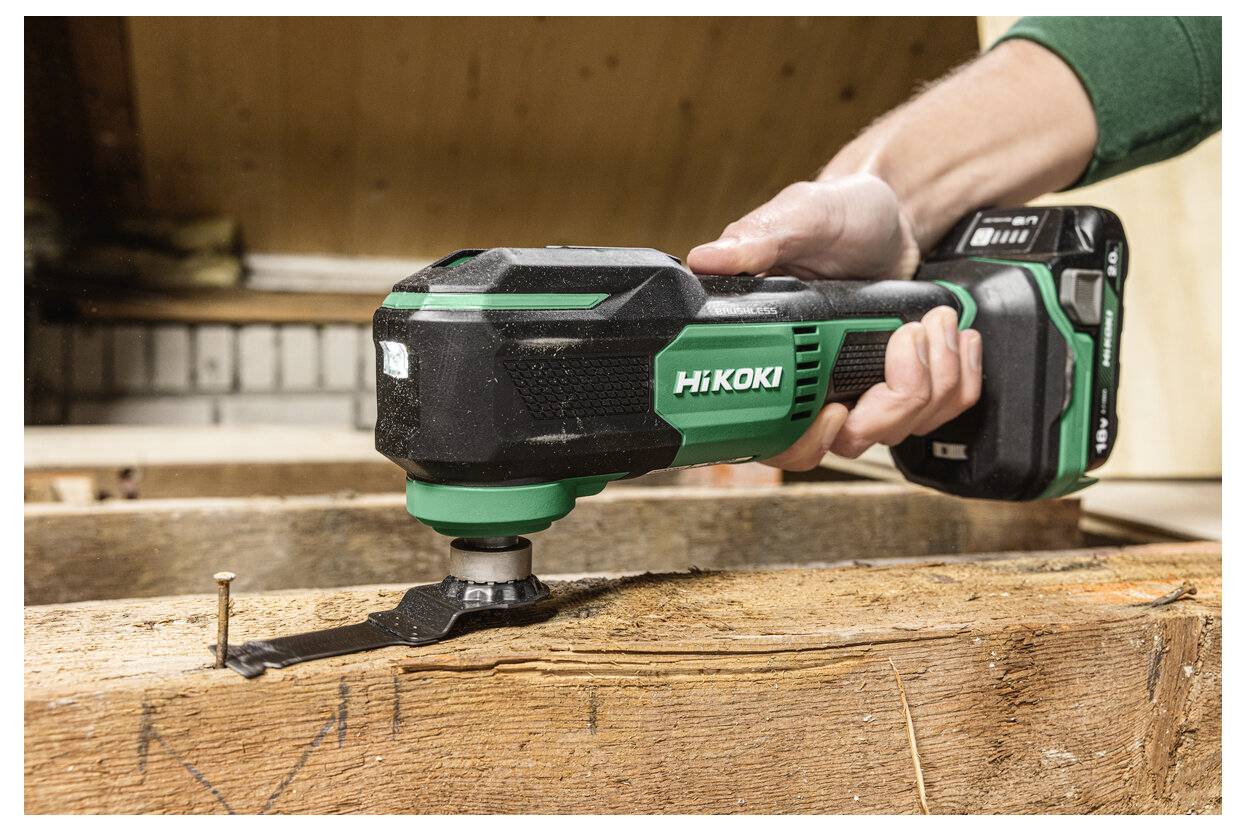 Ręka używa zielonego i czarnego elektronarzędzia marki Hikoki do cięcia drewnianej powierzchni. Gwóźdź jest widoczny na drewnie w pobliżu ostrza.
