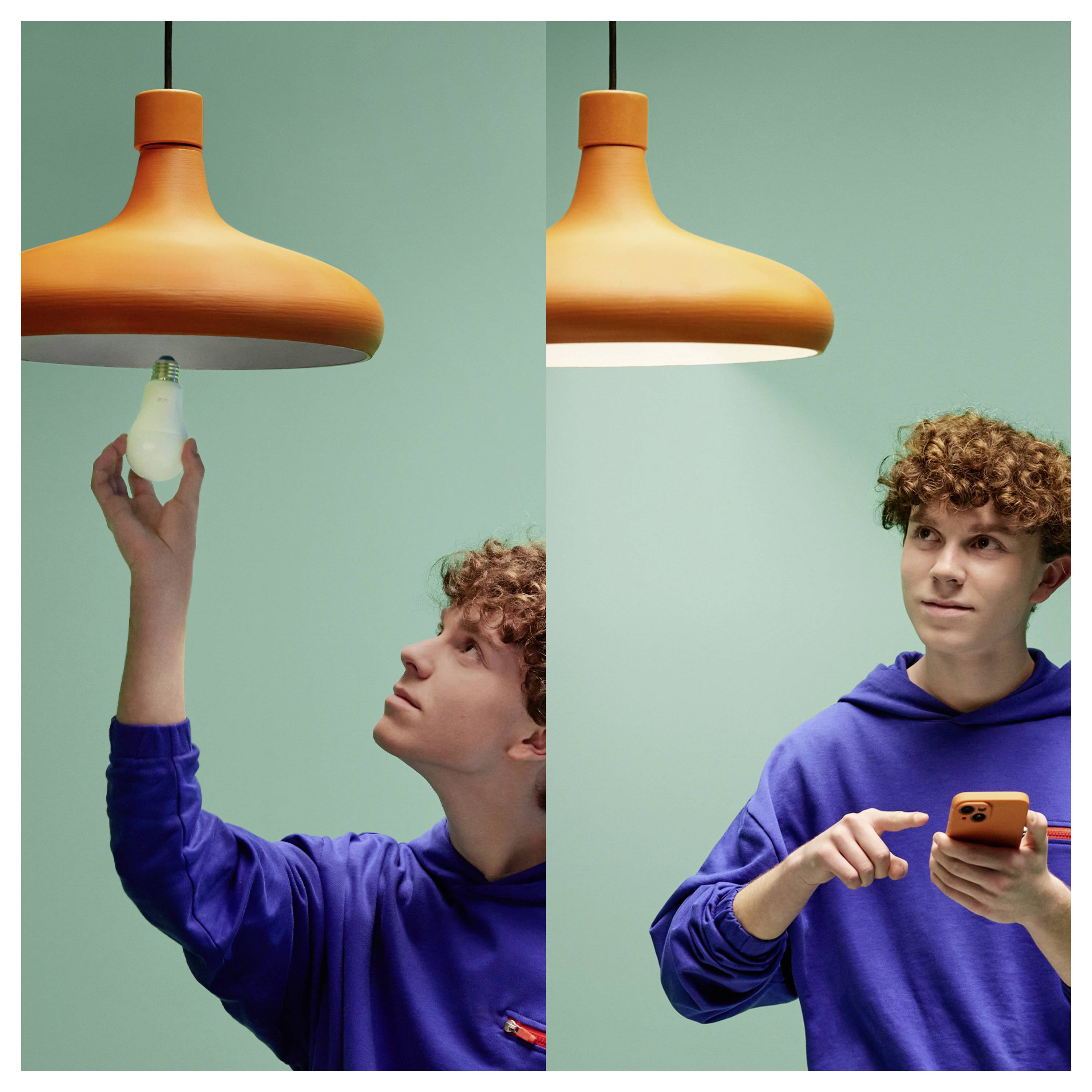 Osoba w niebieskiej bluzie z kapturem zmienia żarówkę w pomarańczowej oprawie sufitowej, a następnie używa smartfona, prawdopodobnie regulując ustawienia.