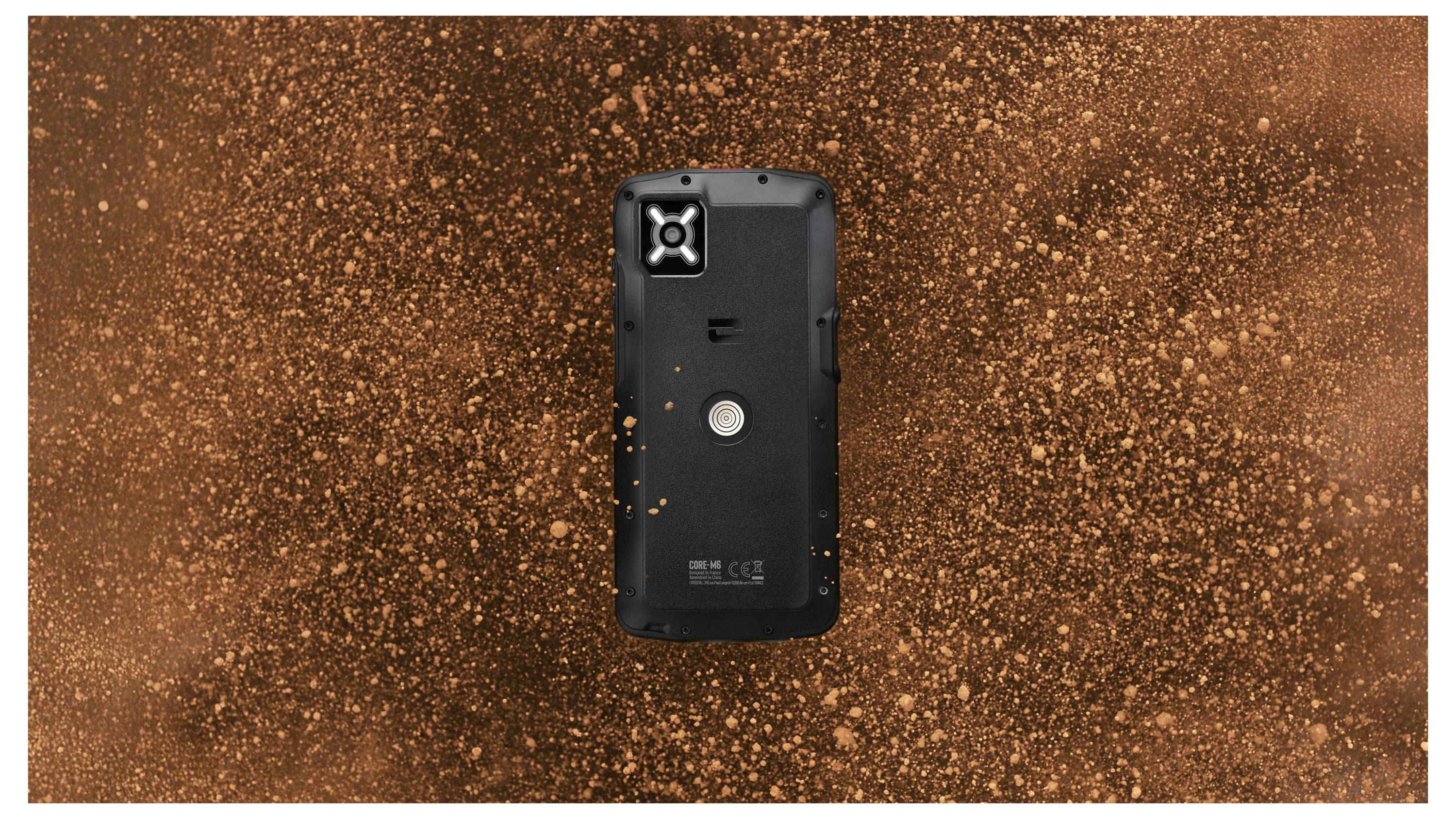 Wytrzymały czarny smartfon z teksturowaną tylną obudową, umieszczony centralnie na dynamicznym, wirującym tle w odcieniach brązu i pomarańczu.