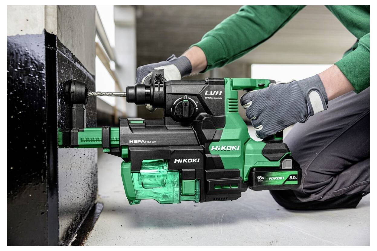Osoba używająca zielonej i czarnej wiertarki przewodowej oznaczonej etykietą 'HiKOKI' do wiercenia w metalowej powierzchni, nosząca przy tym rękawice.