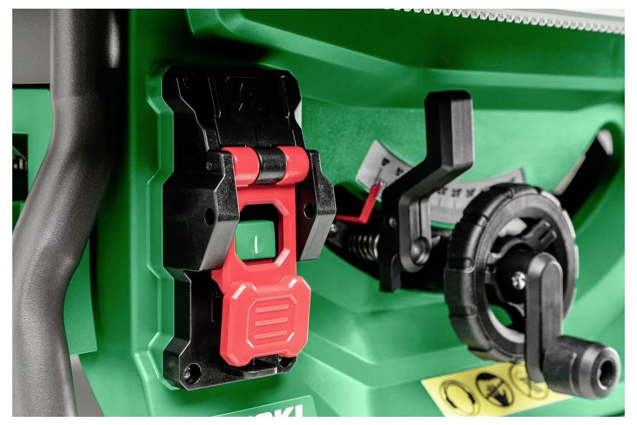 Zbliżenie na czerwony przełącznik bezpieczeństwa i czarną pokrętło regulacyjne piły stołowej, podkreślające jej elementy sterujące i funkcje bezpieczeństwa w warsztacie.