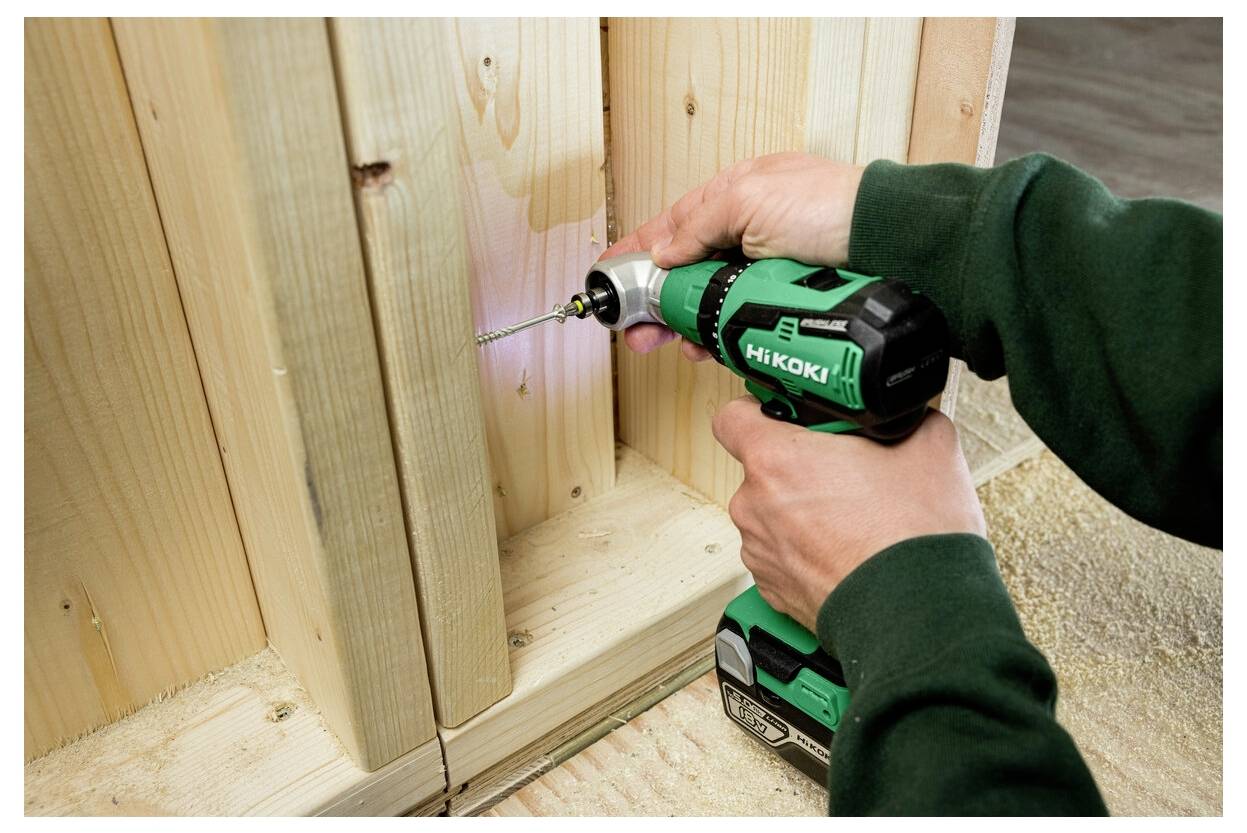 Osoba używa zielonej bezprzewodowej wiertarko-wkrętarki do wkręcania wkręta w drewniane deski. Scena sugeruje prace budowlane lub stolarski.