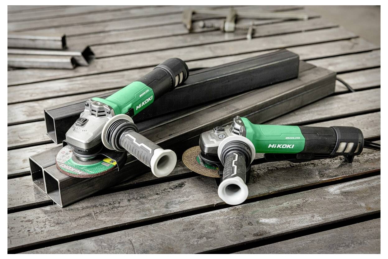 Dwie zielone i szare szlifierki kątowe marki 'Hikoki' spoczywające na metalowych belkach na drewnianej powierzchni, sugerujące prace budowlane lub metalowe.