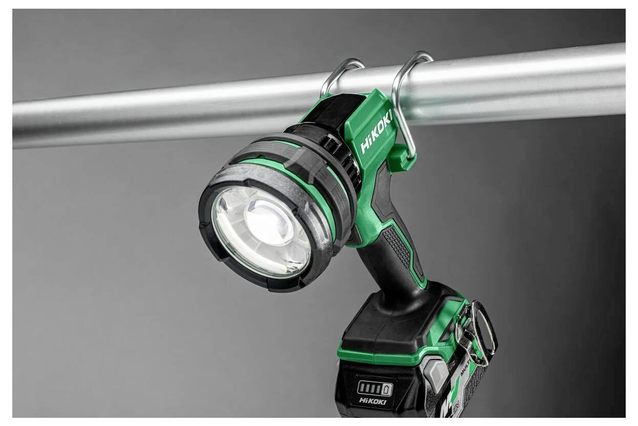 Zielona i czarna latarka z uchwytem wisi na metalowym pręcie za pomocą haka. Latarka jest włączona, rzucając skoncentrowaną wiązką światła.