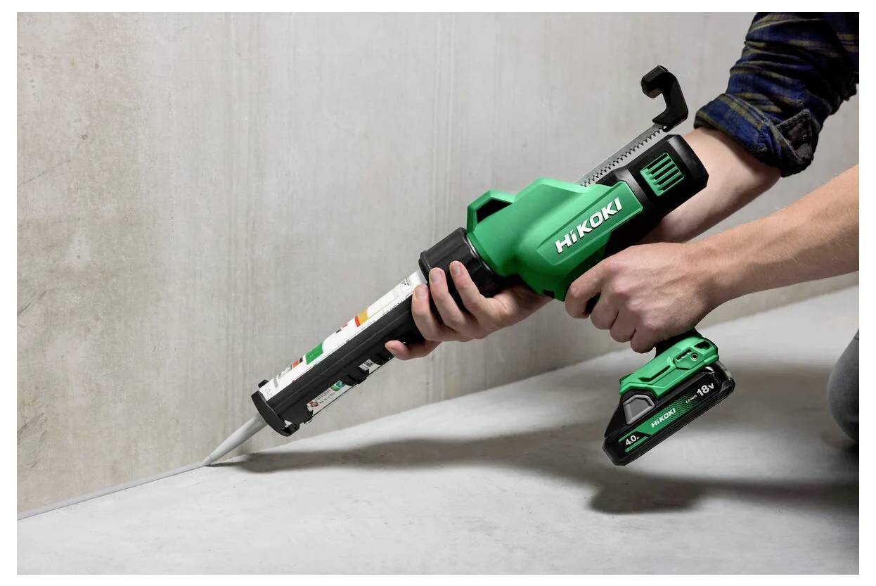Osoba używająca zielonego bezprzewodowego pistoletu do uszczelniania marki HiKOKI nakłada uszczelniacz wzdłuż spoiny betonowej.