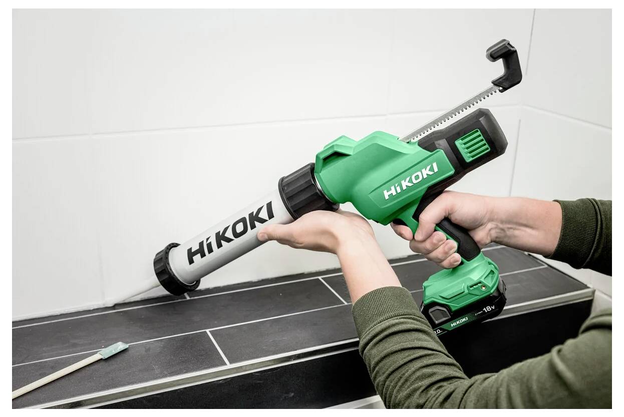 Osoba używa zielonego bezprzewodowego pistoletu do uszczelniania HiKOKI, nakładając uszczelniacz wzdłuż krawędzi powierzchni wyłożonej kafelkami.