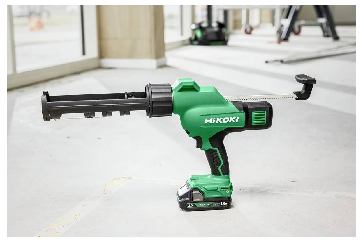 Zielony, bezprzewodowy pistolet do uszczelniania Hikoki na betonowej podłodze w jasnym pomieszczeniu, z dużymi oknami i narzędziami budowlanymi w tle.