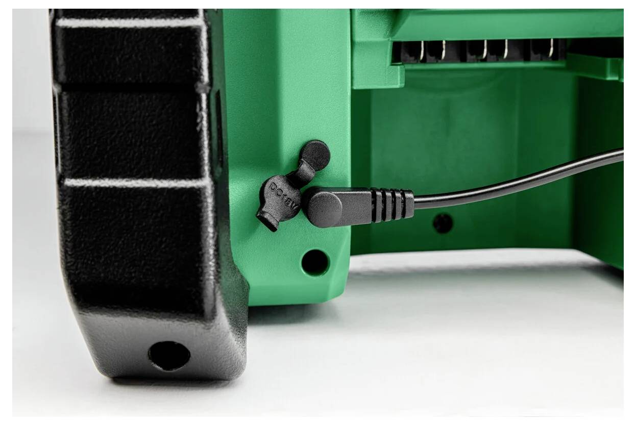 Zbliżenie zielonego urządzenia z czarnym przewodem elektrycznym podłączonym do niego oraz włącznikiem oznaczonym napisem 'Zabezpieczenie'; nacisk na połączenie i funkcjonalność.