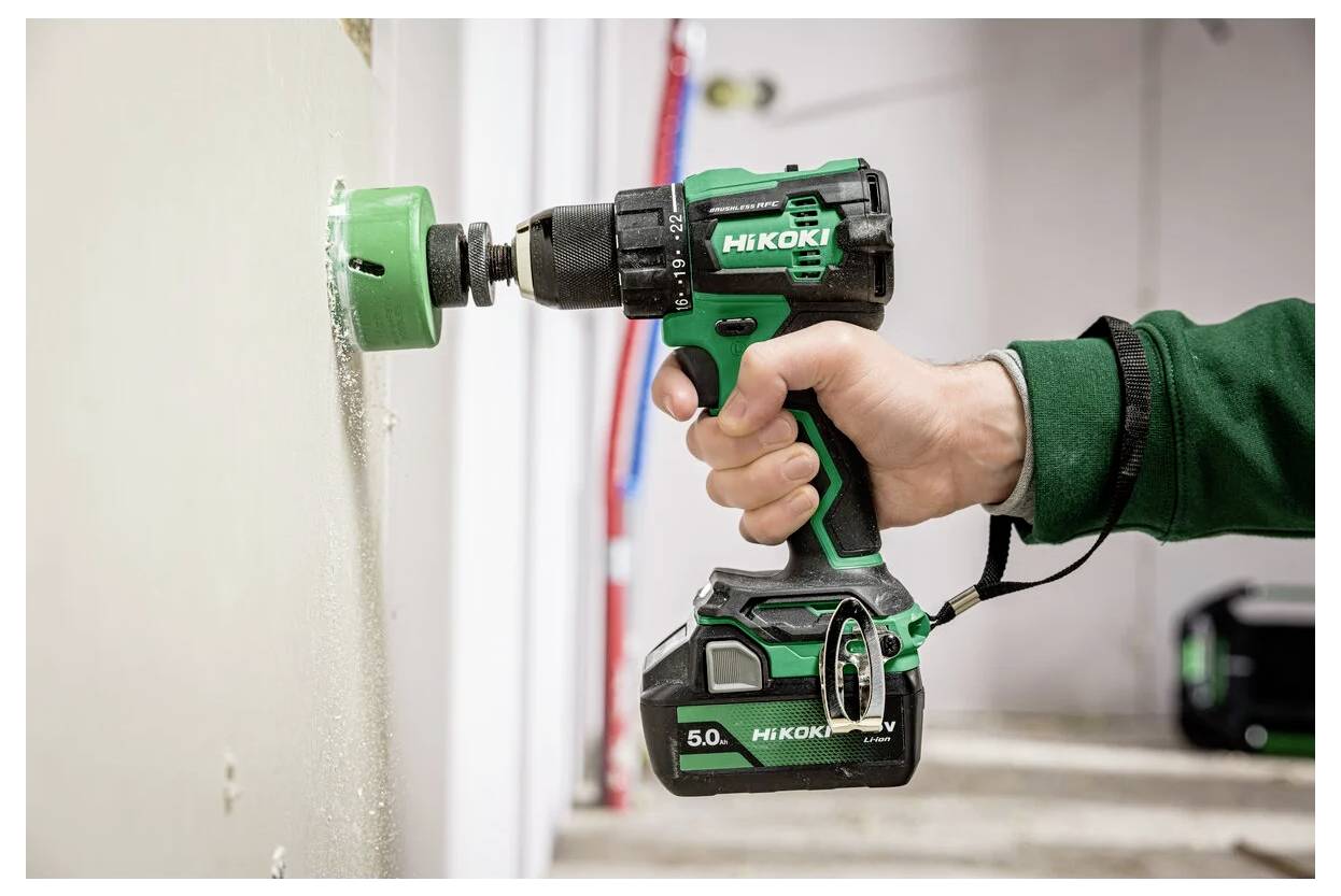 Osoba używa zielonej bezprzewodowej wiertarki do wywiercenia otworu w ścianie wewnątrz budynku.