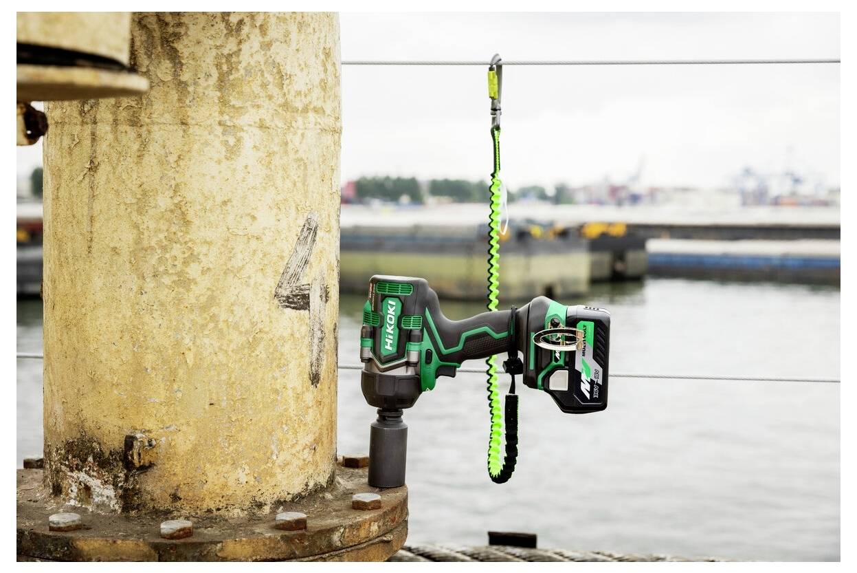 Zielono-czarne narzędzie elektryczne przymocowane do żółtego słupa za pomocą przewodu bezpieczeństwa, w pobliżu nabrzeża z przemysłowym tłem.