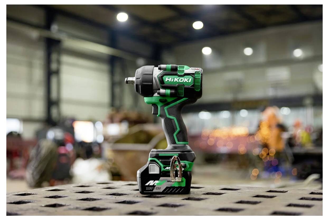 Zielono-czarny bezprzewodowy narzędź elektryczny z firmową etykietą, umieszczony na perforowanej metalowej powierzchni w przemysłowym warsztacie.