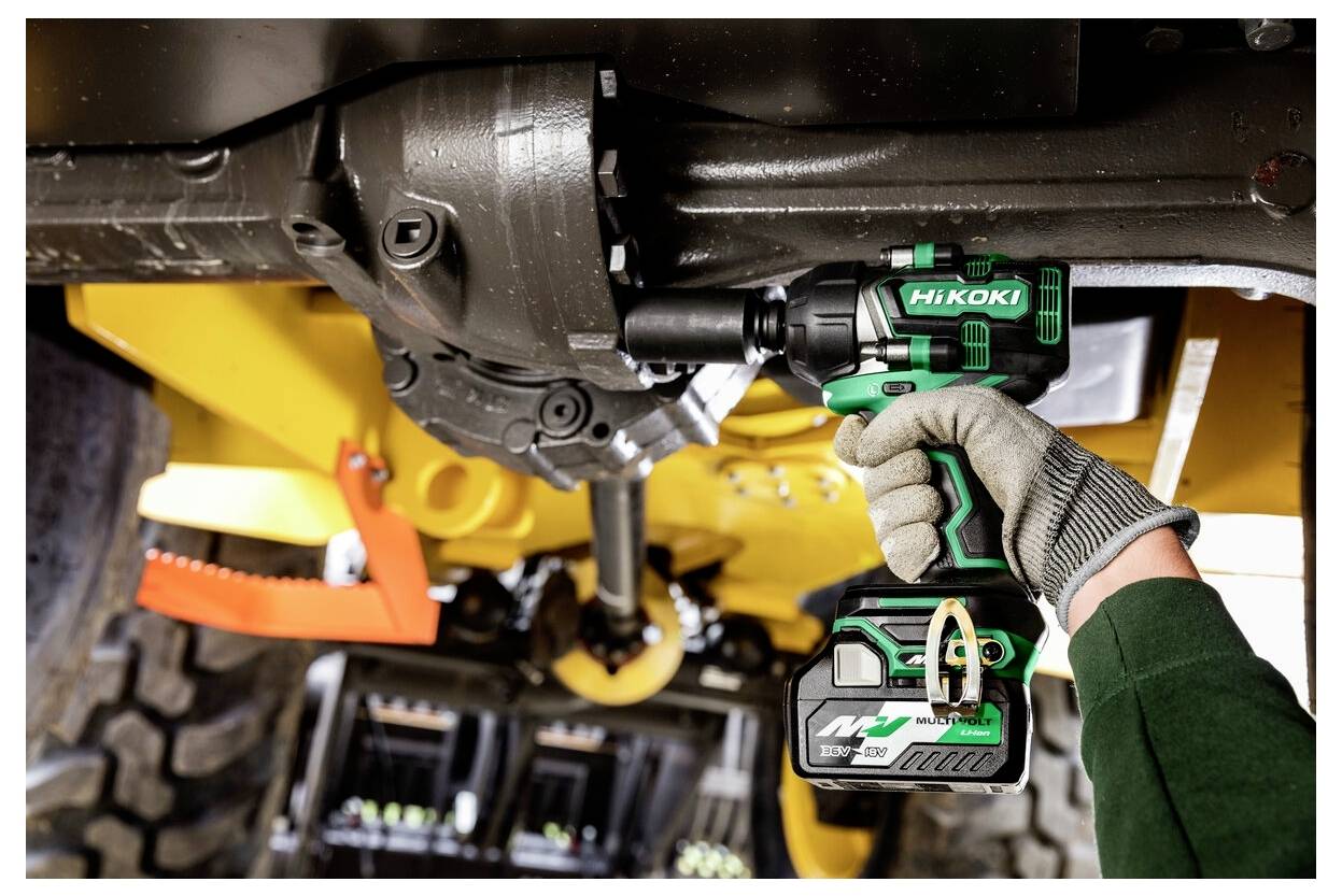 Osoba używa zielonego i czarnego akumulatorowego klucza udarowego HiKOKI, aby dokręcić śrubę pod spodem maszyny budowlanej.