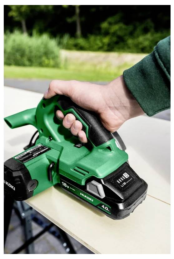 Osoba używająca zielonego ręcznego stolarskiego hebla zasilanego baterią, wygładzająca krawędź drewnianej deski na wolnym powietrzu.