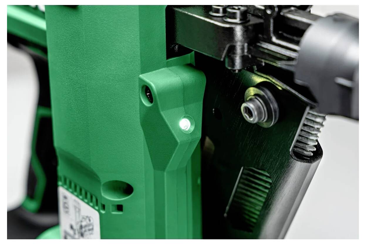 Zbliżenie zielonego narzędzia elektrycznego z podświetlonym wskaźnikiem LED, prezentujące elementy mechaniczne i przyciski sterujące, sugerujące, że urządzenie jest gotowe do pracy.