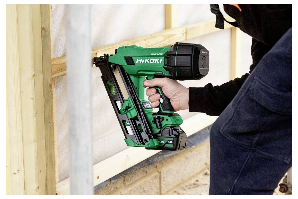 Osoba używa zielonego gwoździarki pneumatycznej, aby zamocować drewniane belki na placu budowy, koncentrując się na precyzyjnym ustawieniu narzędzia.