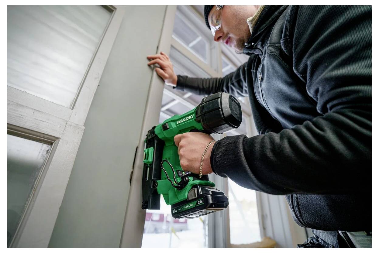 Osoba używa zielonej elektrycznej wiertarki do zamocowania ościeżnicy drzwiowej. Scena sugeruje prace remontowe lub renowacyjne.