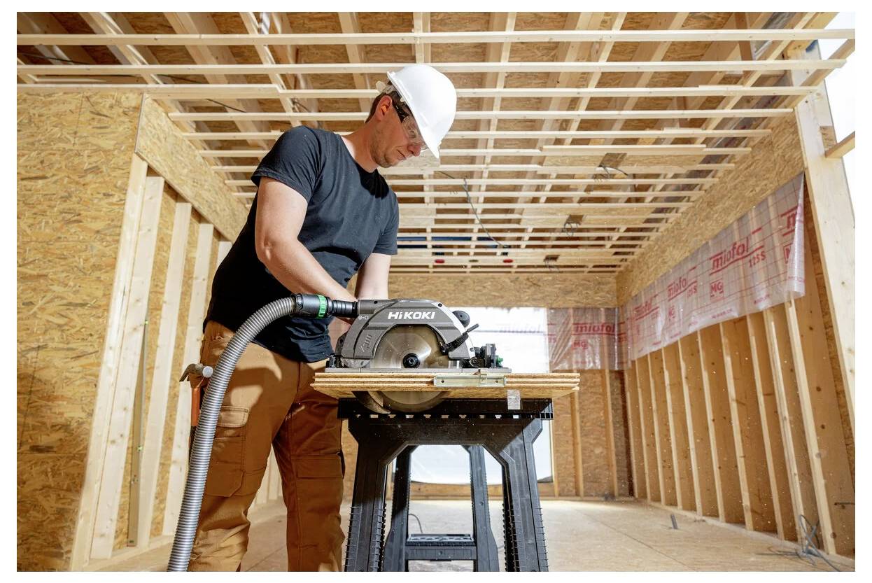 Robotnik budowlany w kasku używa piły tarczowej wewnątrz częściowo zbudowanej drewnianej konstrukcji, koncentrując się na wykonywanej pracy.