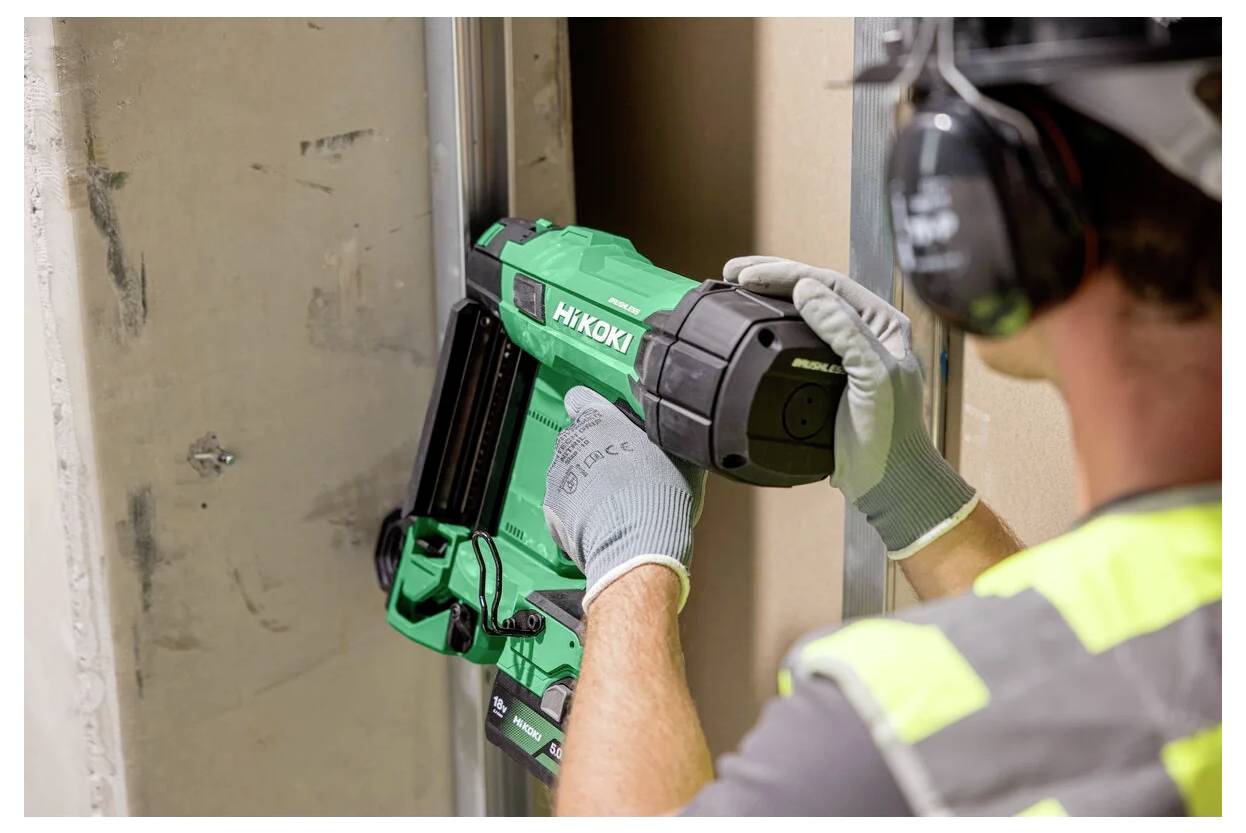 Osoba ubrana w sprzęt ochronny używa zielonego narzędzia elektrycznego do zamocowania panelu na metalowej ramie.