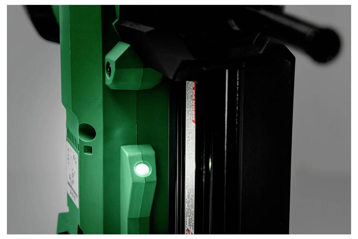 Zielone światło włącza się na fragmencie maszyny, sygnalizując jej stan gotowości do pracy. Urządzenie posiada czarny panel i dźwignię regulacyjną.