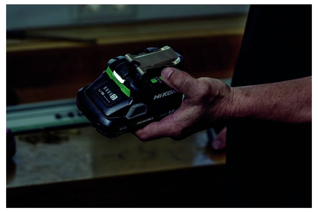 Ręka trzymająca akumulator do elektronarzędzi Hikoki, podkreślająca jego design i rozmiar. W tle nieostry warsztat.