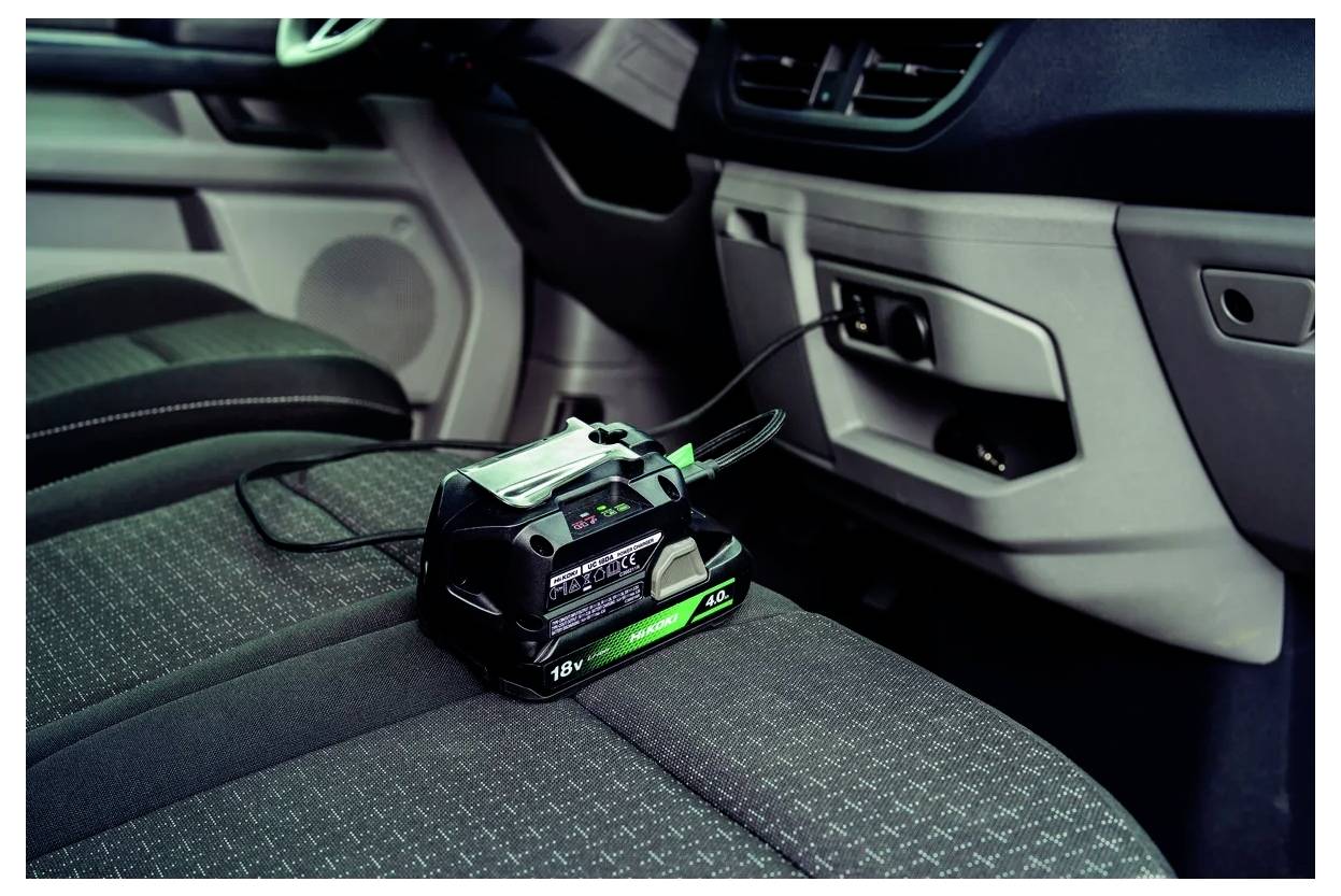 Wnętrze samochodu z przenośną ładowarką akumulatorów podłączoną do gniazda elektrycznego, umieszczoną na fotelu pasażera z przodu.