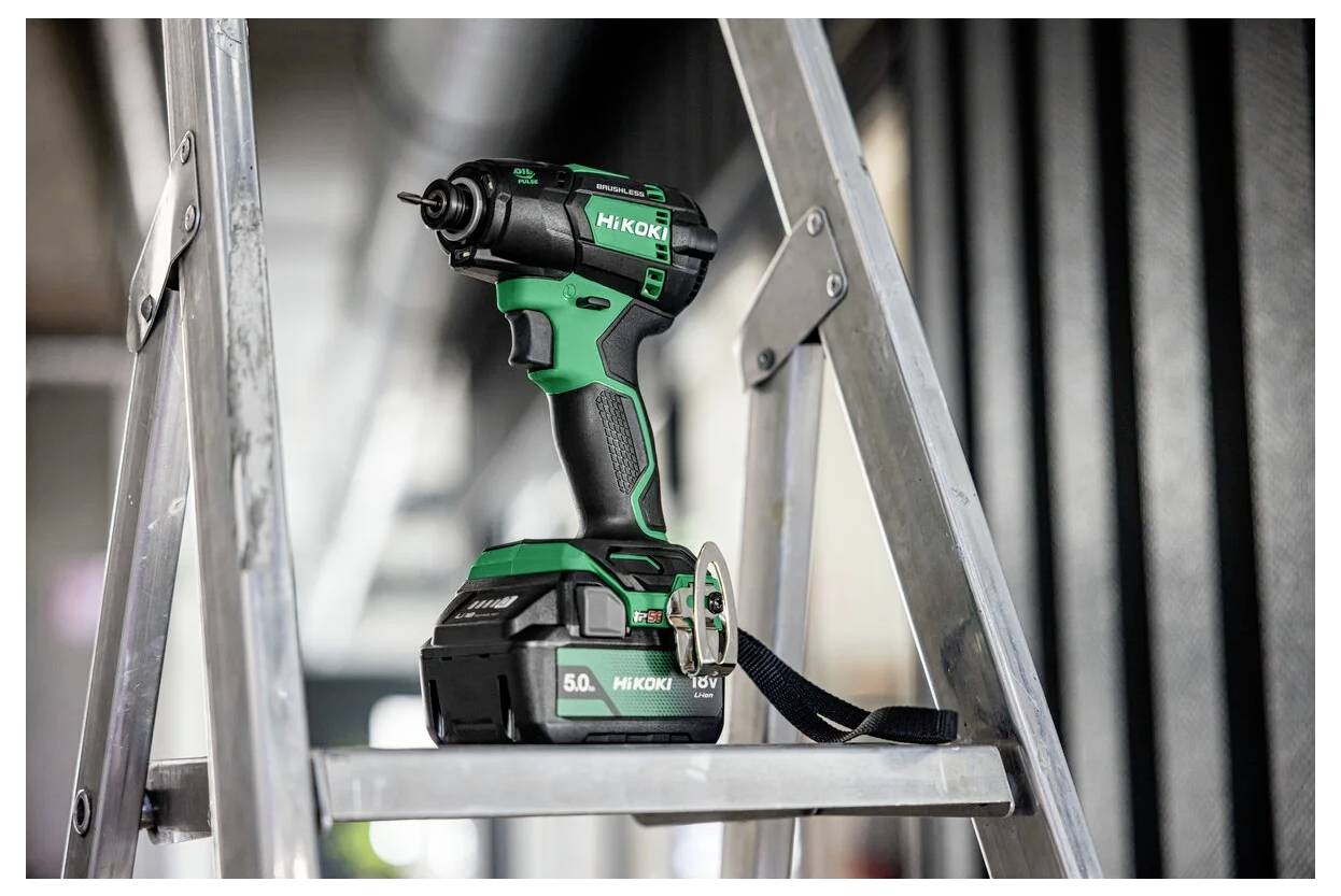 Zielono-czarny akumulatorowy wiertarka oznaczona etykietą 'HiKOKI' leży na srebrnej drabinie, sugerując otoczenie budowy lub prac majsterkowiczowskich.