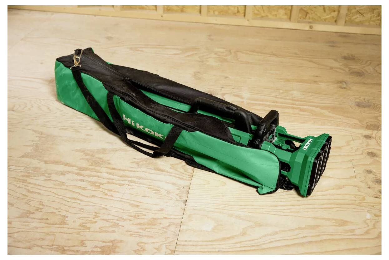 Złożony zielono-czarny statyw stoi na podłodze z płyty pilśniowej, częściowo wsunięty do swojej torby transportowej.