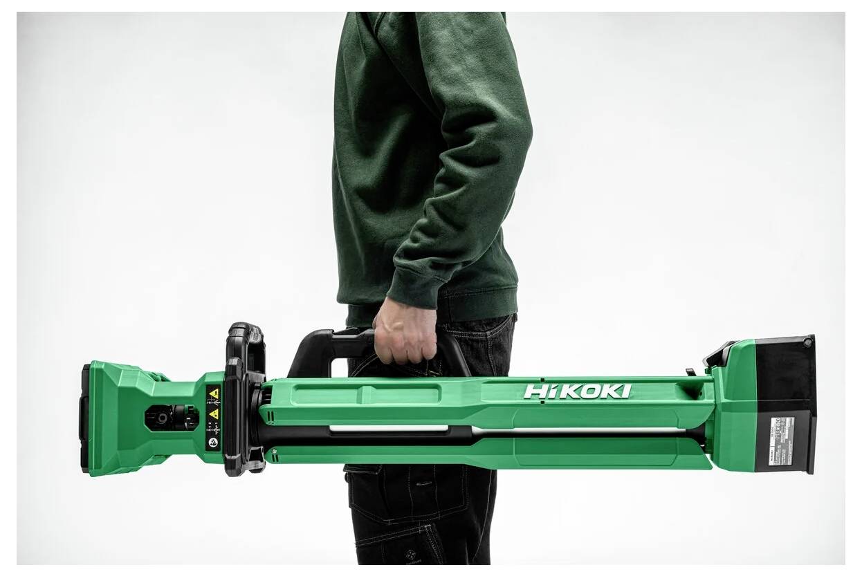 Osoba ubrana w zielony sweter trzyma poziomo zielone elektronarzędzie HiKOKI, prezentując jego rozmiar i projekt na tle jednolitego tła.
