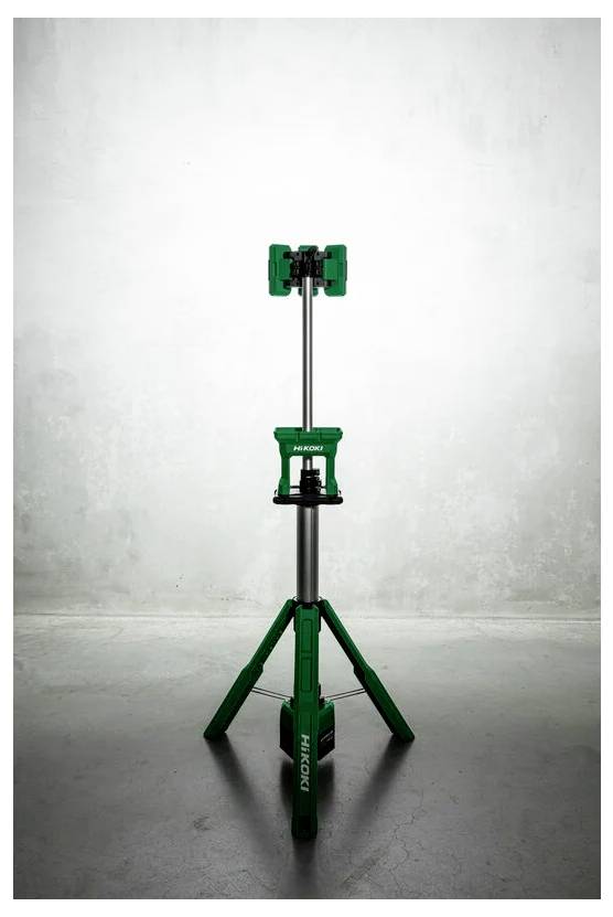 Zielony i srebrny statyw o regulowanej wysokości stoi na betonowej podłodze przy teksturowanej szarej ścianie.