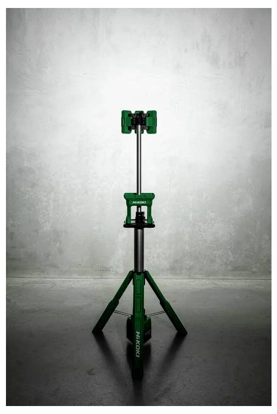 Zielony trójnożny reflektor budowlany stoi na betonowej podłodze, na tle teksturowanej szarej ściany, z widocznym oznakowaniem marki 'Hi Koki'.