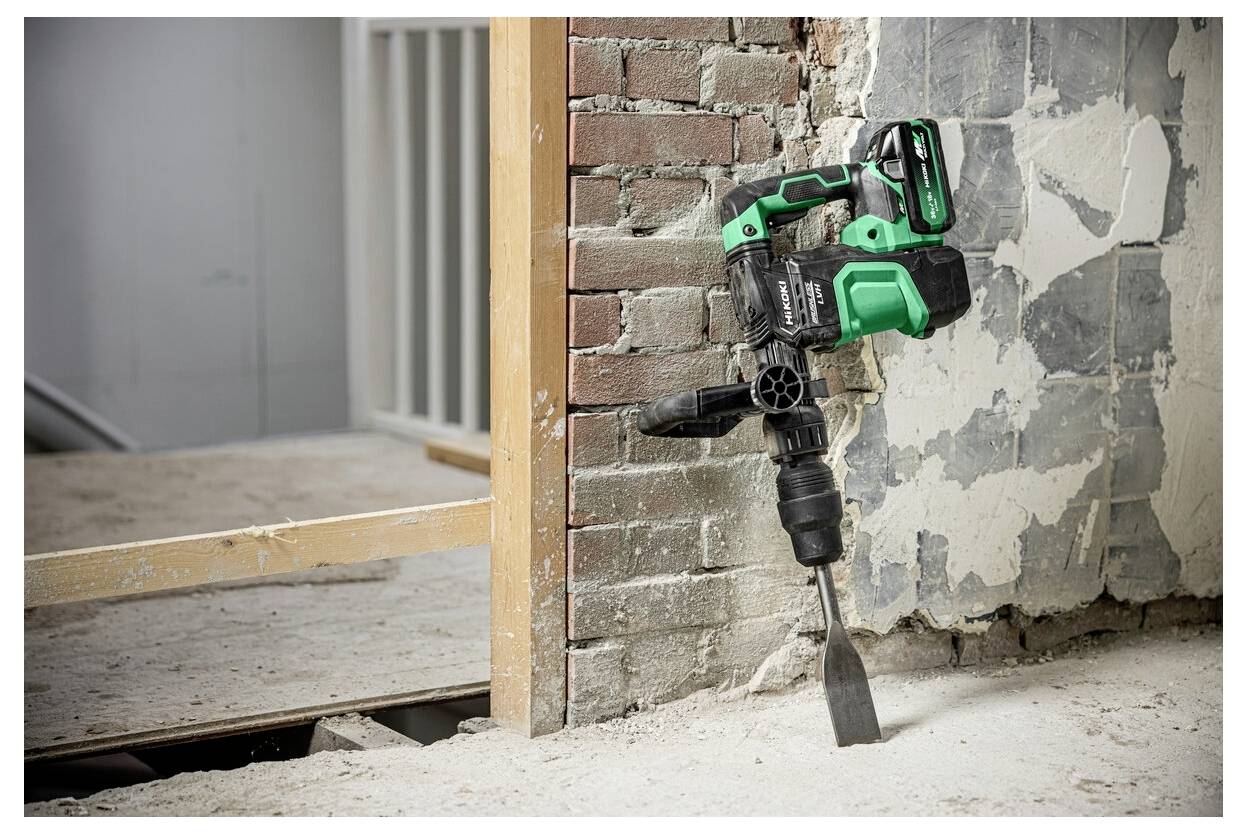 Zielono-czarne narzędzie elektryczne z dłutem jest używane do usuwania tynku ze ściany z cegły, odsłaniając jej podstawową strukturę.