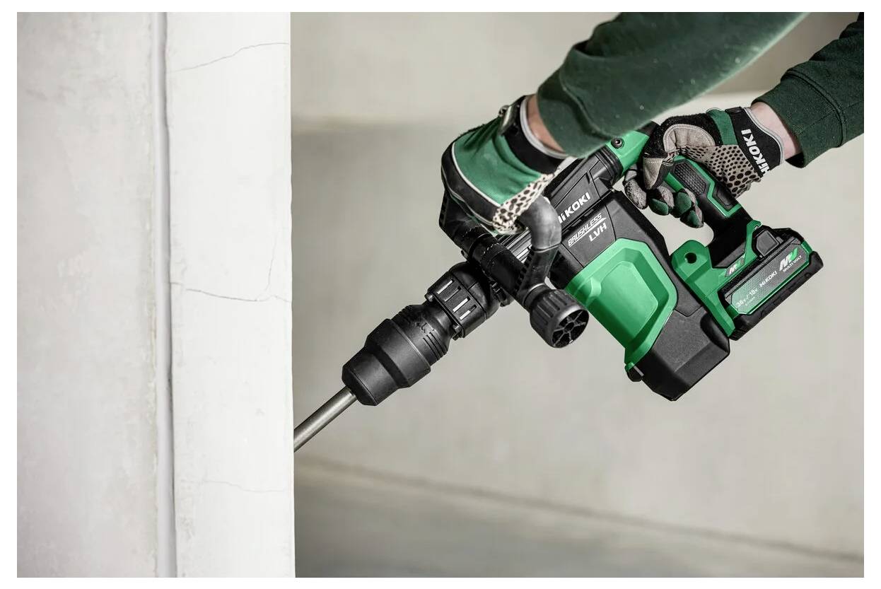 Osoba w rękawicach używa zielonego i czarnego bezprzewodowego wiertła, pracując na betonowej powierzchni, koncentrując się na metalowym wiertelniku.