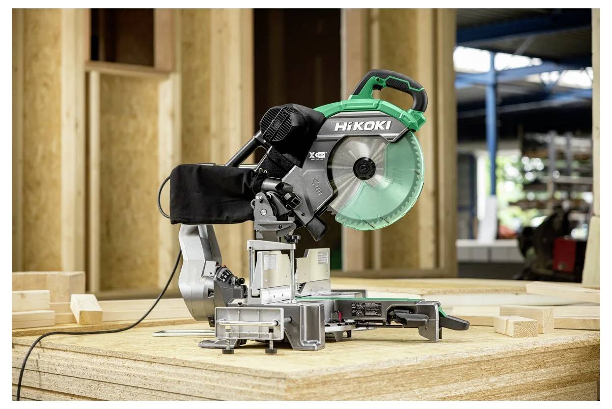 Piła ukośnica na drewnianym stole w warsztacie, otoczona dużymi panelami i belkami drewnianymi, przygotowana do zadań związanych z cięciem.