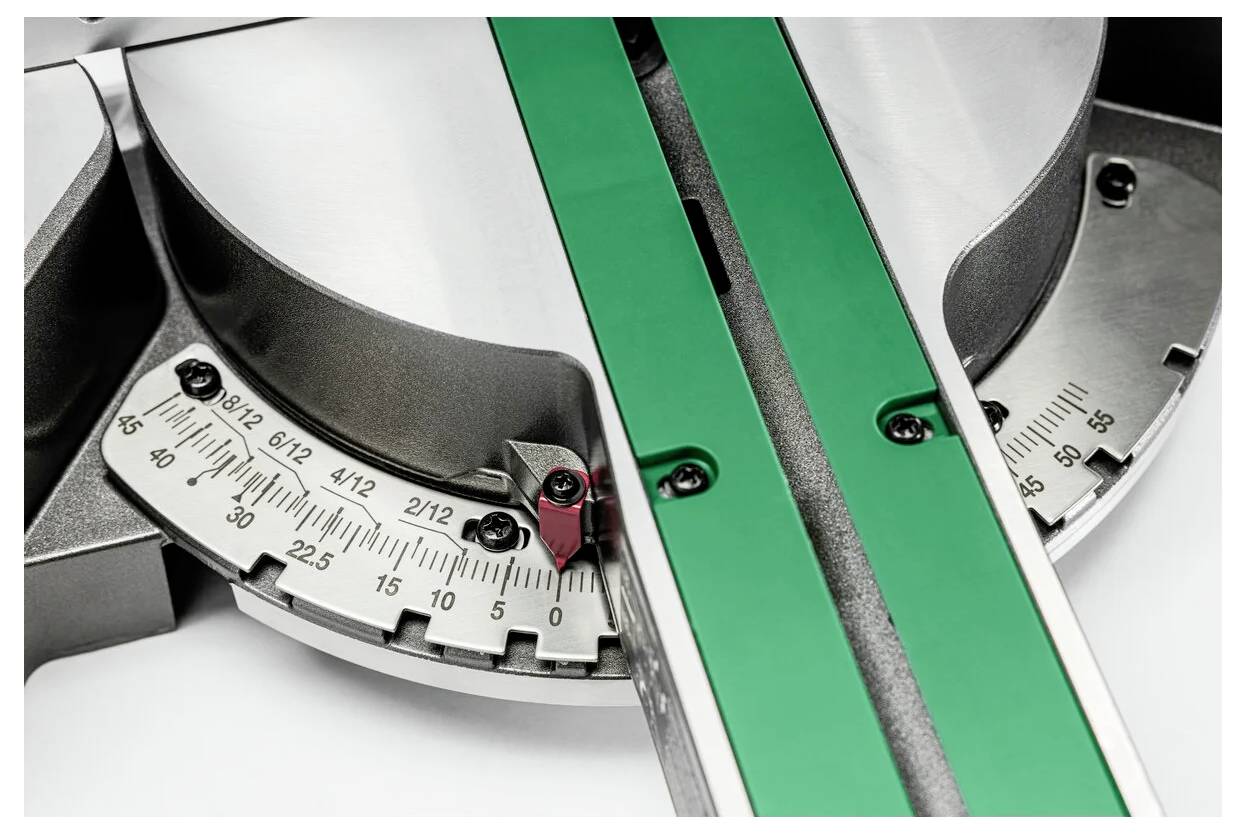 Obraz przedstawia metalowy kątomierz z precyzyjnymi oznaczeniami kątów, z zieloną belką przebiegającą przez jego powierzchnię, prawdopodobnie będącą częścią narzędzia pomiarowego.