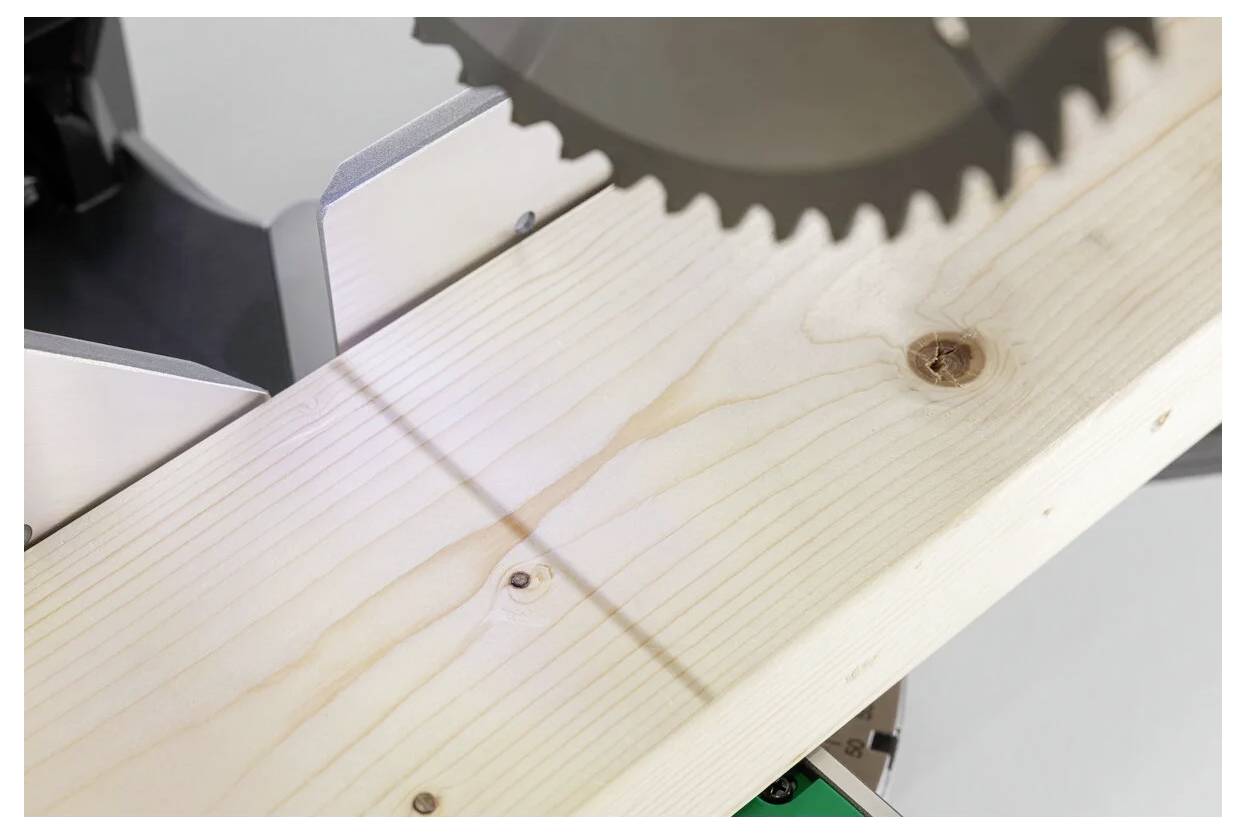 Tarcza piły tarczowej zbliża się do deski sosnowej, ustawionej do cięcia, w przestrzeni warsztatu.