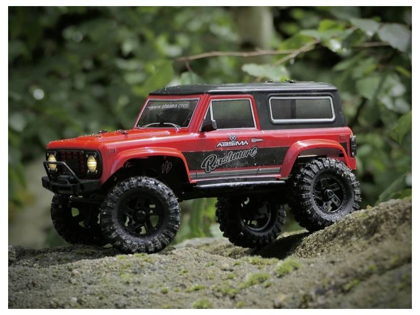 Czerwono-czarny zdalnie sterowany pojazd terenowy na drodze gruntowej otoczony zieloną roślinnością.