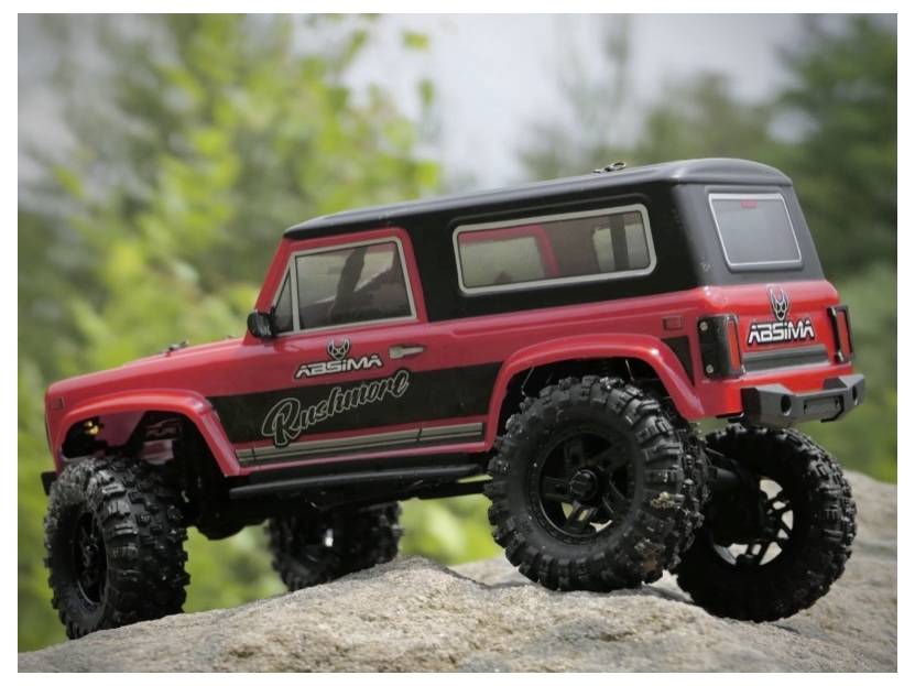 Czerwony zdalnie sterowany pojazd terenowy z dużymi oponami jest pokazany na skale, na rozmytym naturalnym tle.