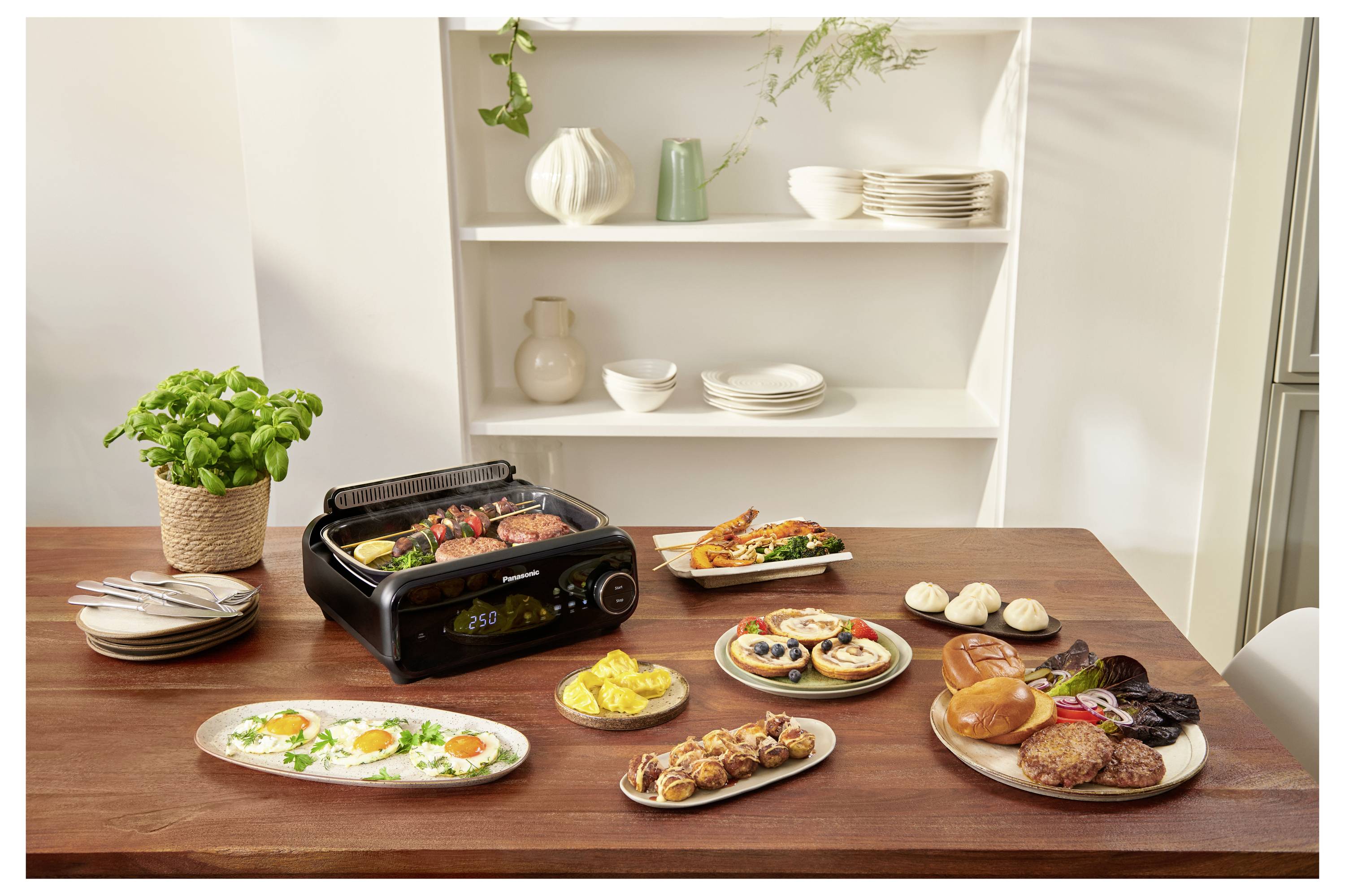 Różne dania gotowane wystawione na stole z grillem. W tle półki z białymi talerzami, miskami i dekoracyjnymi wazonami.