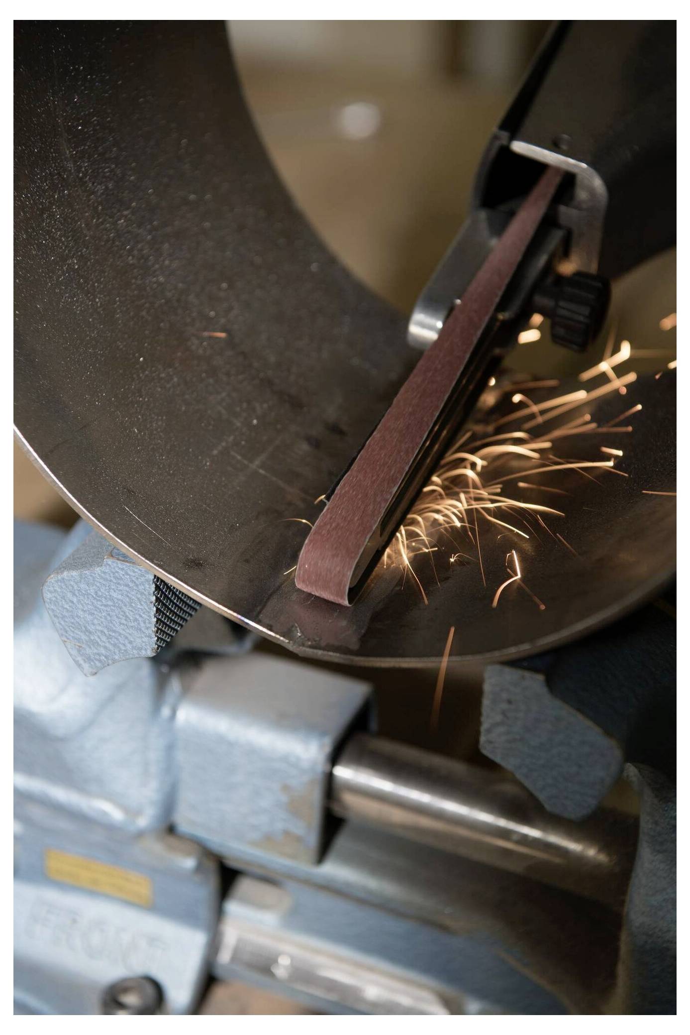 Szlifierka taśmowa wygładzająca metalową powierzchnię z widocznymi iskrami lecącymi w powietrzu, co wskazuje na aktywne szlifowanie i tarcie.