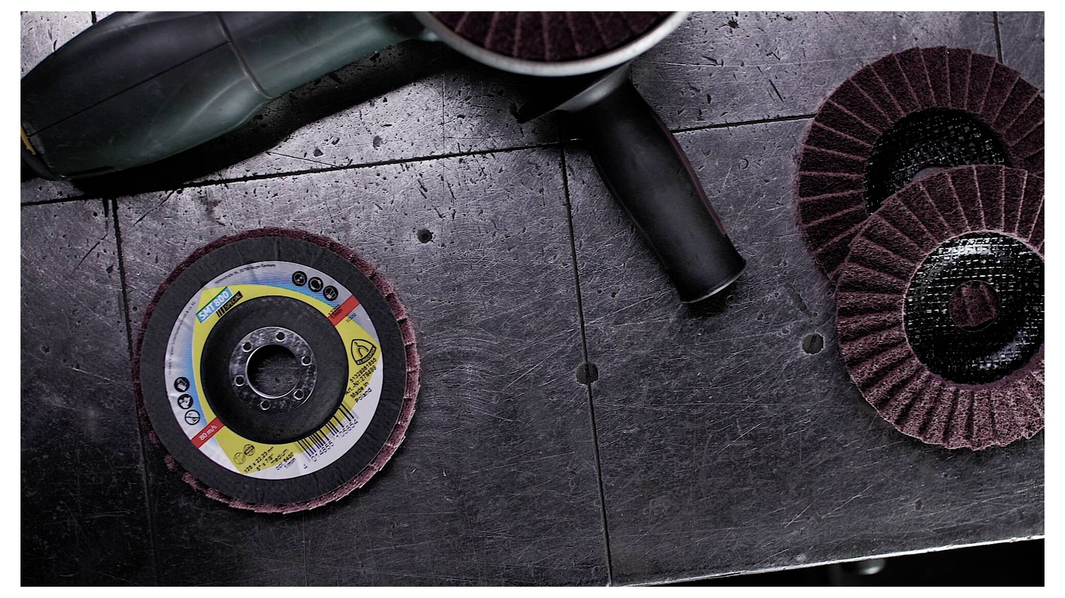 Szlifierka kątowa na metalowym stole warsztatowym z tarczami szlifierskimi, podkreślająca narzędzia do obróbki metalu i zadań związanych z wykańczaniem powierzchni.