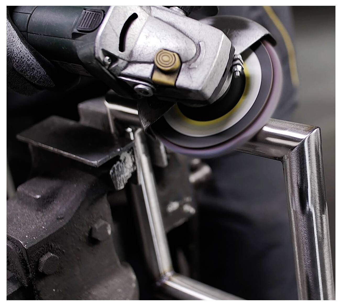 Osoba używa szlifierki kątowej do polerowania metalowej krawędzi prostokątnej ramy, wywołując przy tym iskry.