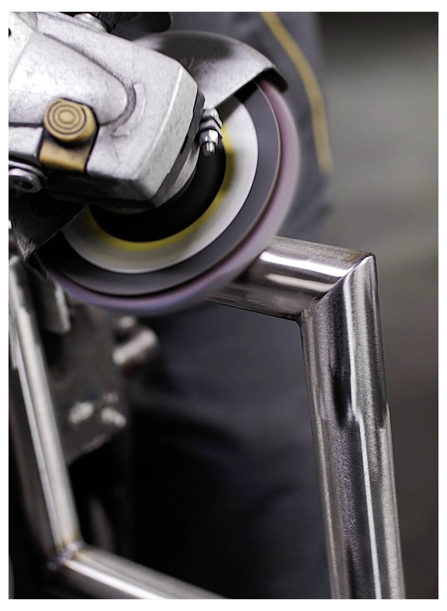 Osoba używa szlifierki kątowej do polerowania rogu metalowej ramy, tworząc gładką, błyszczącą powierzchnię.