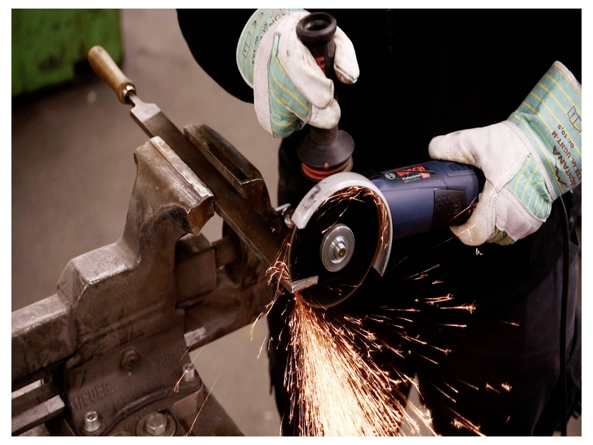 Pracownik używa szlifierki kątowej na metalu, tworząc jasne iskry. Pracownik nosi rękawice ochronne i mocno trzyma narzędzie przy metalu.