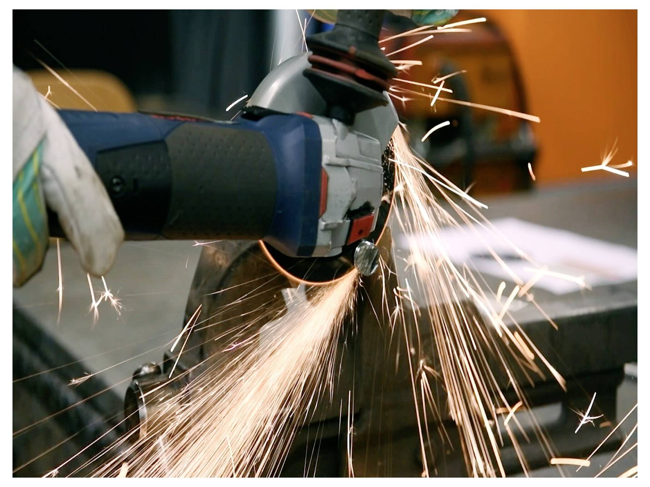 Robotnik używa szlifierki elektrycznej, powodując wyrzucanie iskier podczas cięcia metalu, co wskazuje na proces obróbki metalu.