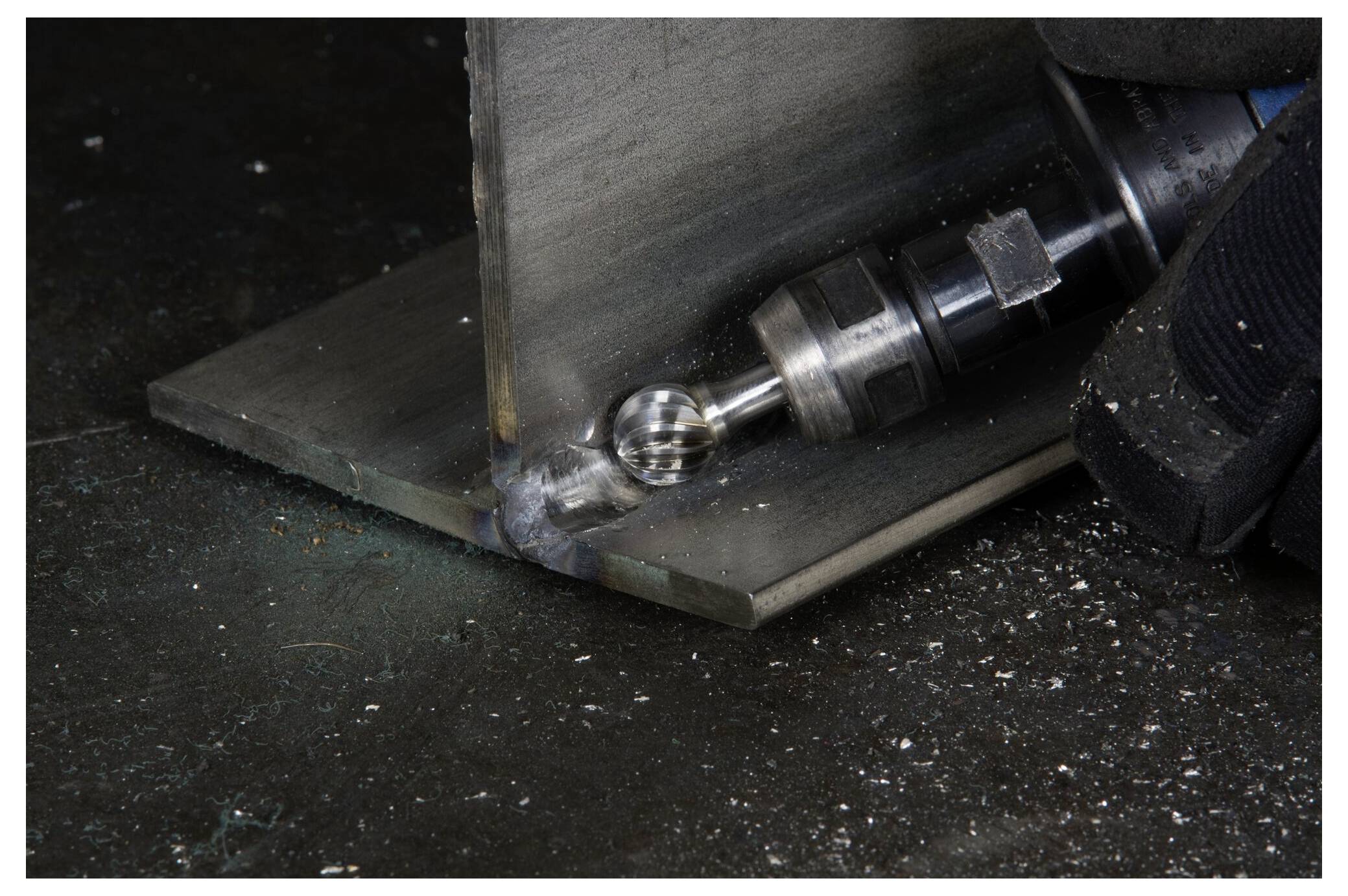 Osoba używająca narzędzia obrotowego z frezem z węglika spiekanego do szlifowania spoiny metalowej na skośnej strukturze blachy, tworząc gładkie krawędzie.