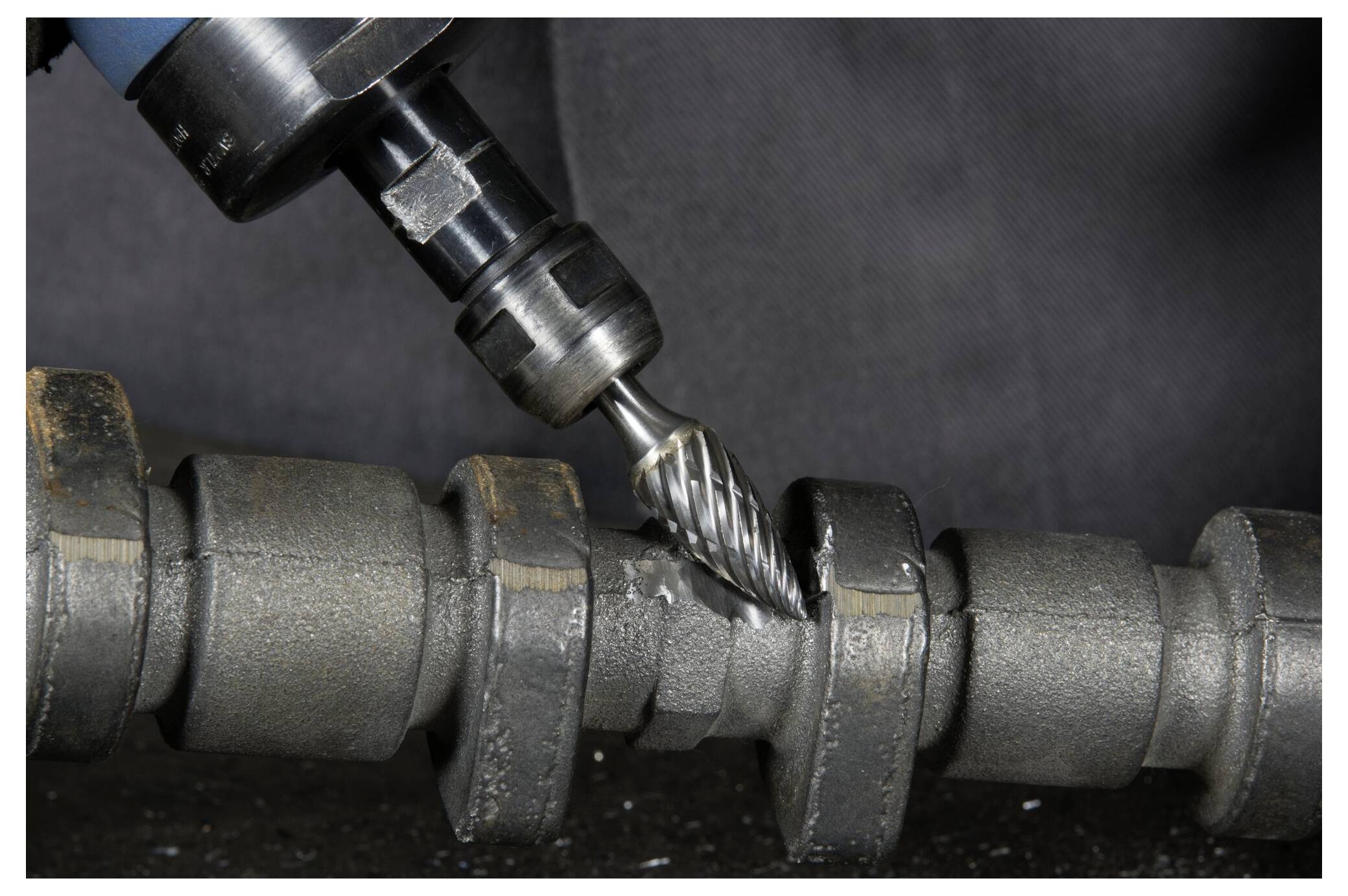 Metalowa frezarka precyzyjnie wycina rowki w cylindrycznym elemencie metalowym na ciemnym tle.